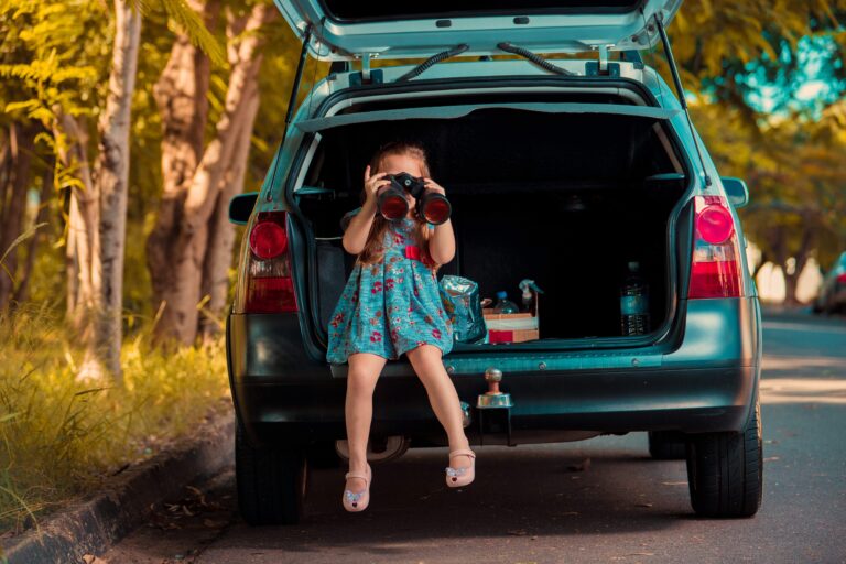 An image of a child sitting backside on the car and trying to capture an image. for traveling with children