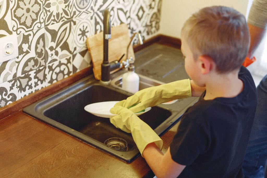 An image of a child washing dishes. Helping is one of a good habits.