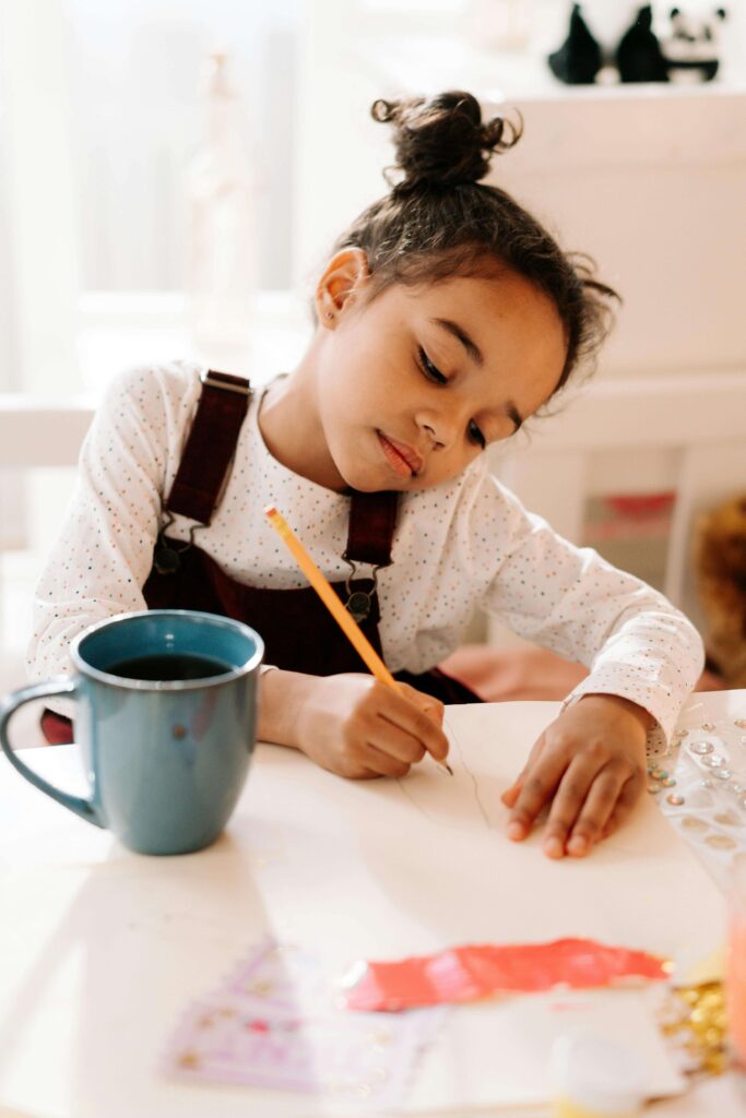 "Image: A child sits at a desk, pen in hand, engaged in journal writing. The journal is open, revealing colorful pages with 'journaling prompts' printed on them. The child appears focused and thoughtful as they explore the prompts, fostering creativity and self-reflection."