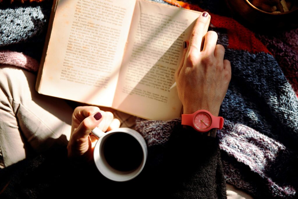 An image of a mother reading a book on parenting with a cup of tea.