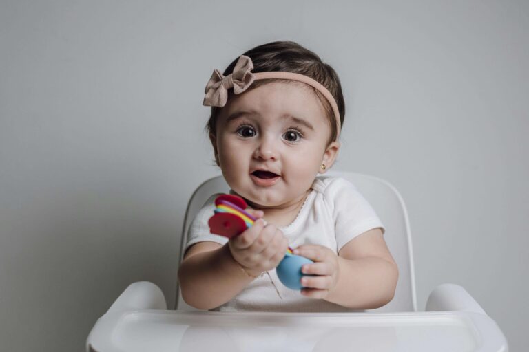 An image of an infant child holding toys in her hands that helps building fine motor skills.