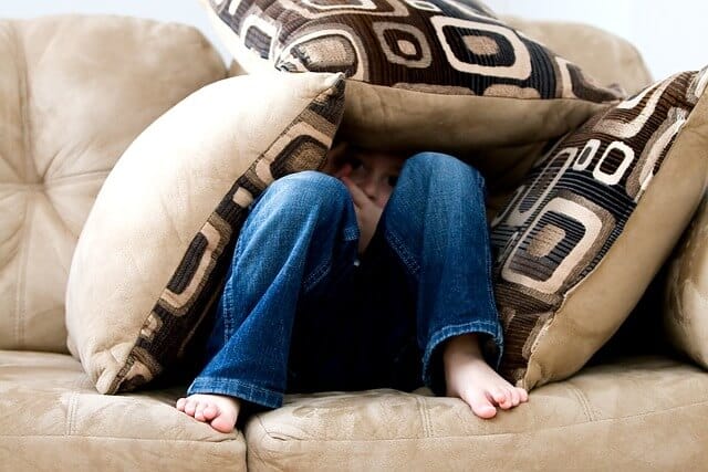 An image of a child child hidden under the cushions shows no patience as an adhd child and playing non stop.