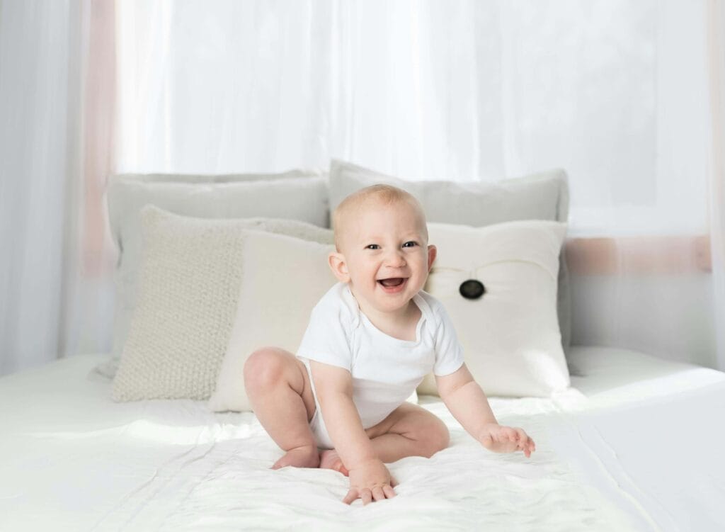 An image of a toddler sitting on a bed with the support of pillows. It shows that toddler is not ready for the bed now.